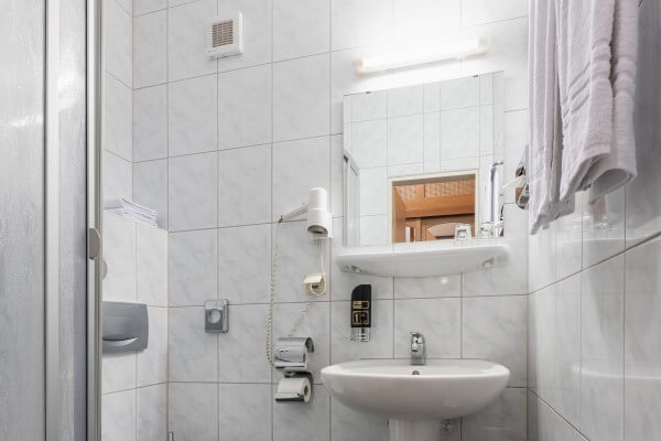 Waschbecken, Toilette und Dusche mit weißen Fliesen und Handtüchern