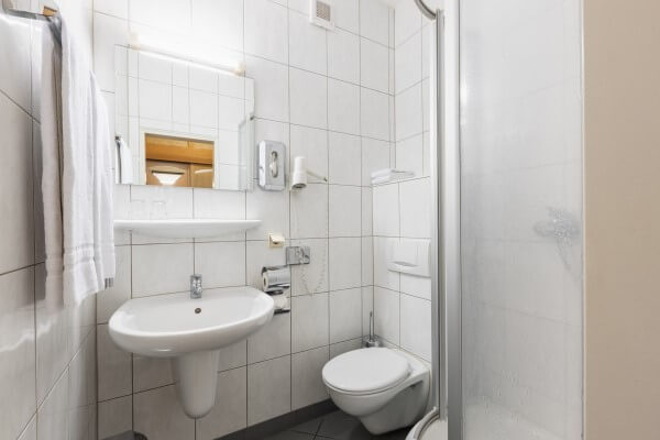 Standard Badezimmer mit weißen Fliesen und Waschbecken, WC und Dusche.