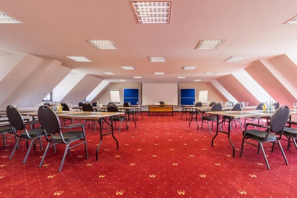 Konferenzsaal für Tagungen und Weiterbildungen mieten und Tische und Stühle umstellen auf rotem Teppich.